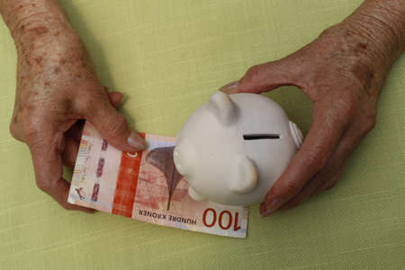 hands of an older woman holding norwegian banknote and piggy bank