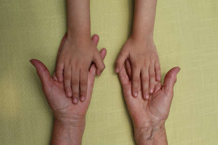 hands of an elderly woman holding the hands of her granddaughterの写真素材