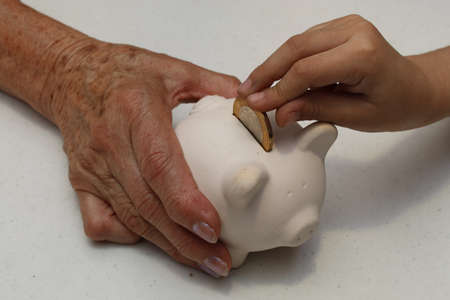 hand of an older woman holding a piggy bank and hand of a girl depositing mexican coin