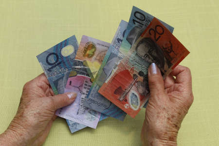 hands of an older woman holding and counting australian banknotes
