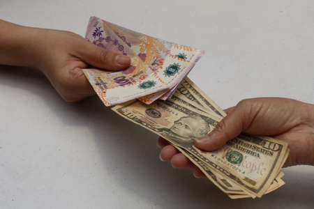hands exchanging argentine banknotes and american dollars bills