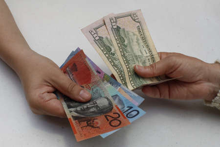 hands exchanging australian banknotes and american dollars bills