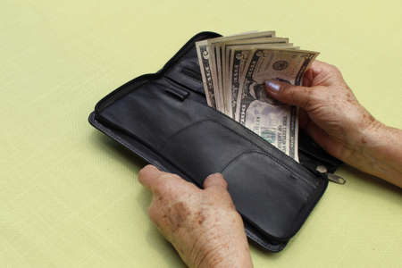 hands of an older woman holding american dollars bills and black leather walletの写真素材