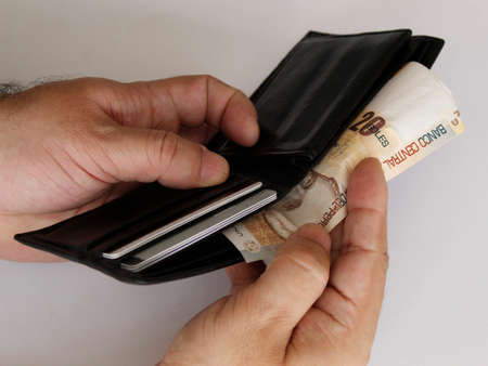 hands of a man holding peruvian banknote and a black leather wallet