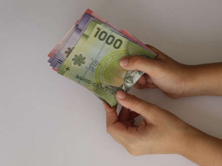 hands of a young woman holding and counting chilean banknotes