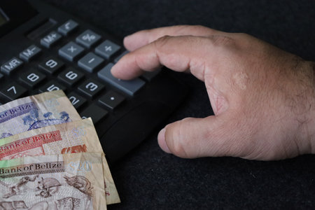 Belizean banknotes of different denomination with hand of a man and calculator on the tableの写真素材