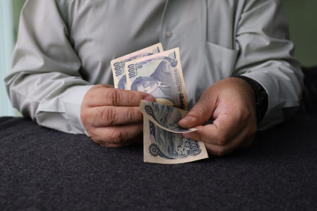 hands of a man holding and counting japanese yen banknotes