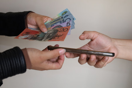 hands of two women paying with Australian banknotes and receiving a smartphone