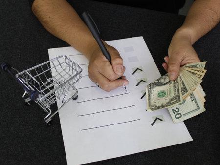 hands holding american money with a shopping cart and writing down a to do list