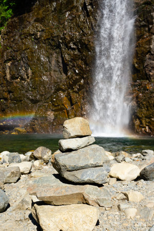 Cairn in front of a rainbow and waterfallの写真素材