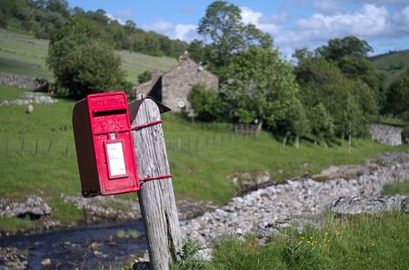 Red postbox clinging to a wooden post by the side of a country road in the Yorkshire Dales.の写真素材