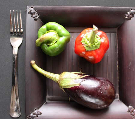 Fresh baby vegetables over black plate and forkの写真素材