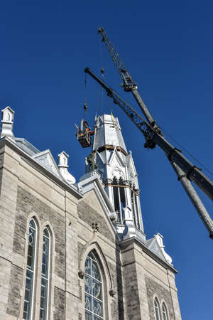Repair of the steeple of the church of Saint-Pie in Quebec, Canada with two cranesの写真素材