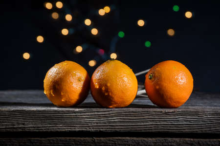 A row of three oranges clementines on a barn wood board with background lights on a black backgroundの写真素材