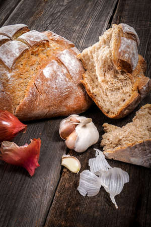 Country bread with pieces of crumb, garlic cloves and french dry shallots on a barn wood board