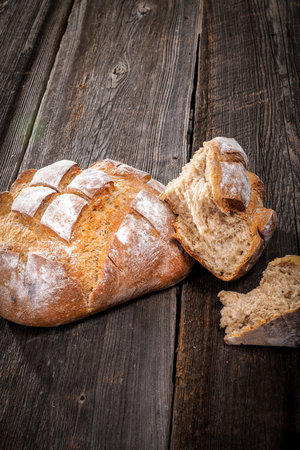 Country bread with floured crust with pieces of crumb on a barn wood board on white backgroundの写真素材