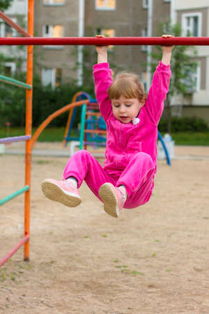 A little girl is hanging on a bar and smiling. Healthy lifestyleの写真素材