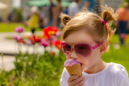 The girl in fashion glasses is eating ice cream. Child and delicious ice cream. Face smeared in ice creamの写真素材