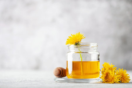 Glass honey jar, dandelion flower and wooden honey dipper. Copy space