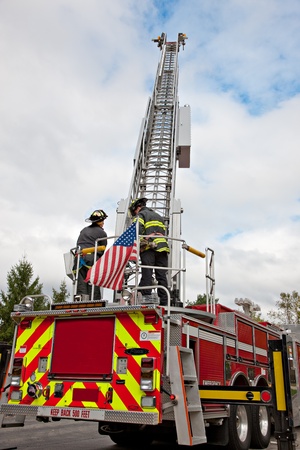 Two Firefighters operate on fire truck in summer clear sky
