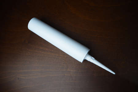 Sealant cartridge on the table. White caulk on wood table. Sealant for fix water leak.の写真素材