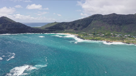 Flying over Makapuu Beach Park. Giant waves foaming and splashing in the ocean. The turquoise color of the Pacific Ocean water on tropical island. Magnificent mountains of Hawaiian island of Oahu.の写真素材