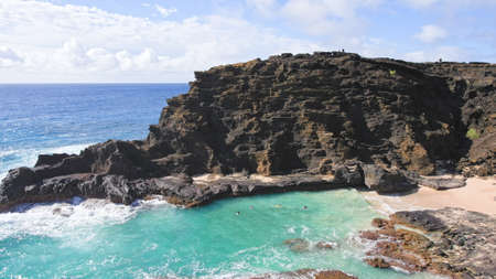 People swim in the turquoise waters of the Tropical Beach. Halona Beach Cove. Blue Waves of the Pacific Ocean Beats Oahu Island Volcanic Cliffs. Clear sunny day. DCI 4kの写真素材