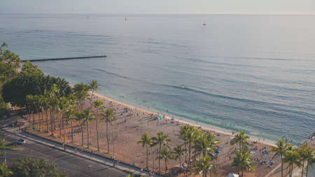 Tourists enjoy the warm sun on a tropical beach. Amazing sunset at Waikiki beach. Hawaiian Island Oahu. Biruse waves of the Pacific Ocean.の写真素材