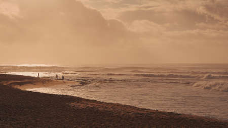 Dramatic sunrise over the ocean. Sandy coast of Oahu island, Hawaii. People walk along the beach. A...