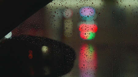 Raindrops run down the glass of the car against the backdrop of the bright lights of the night city....