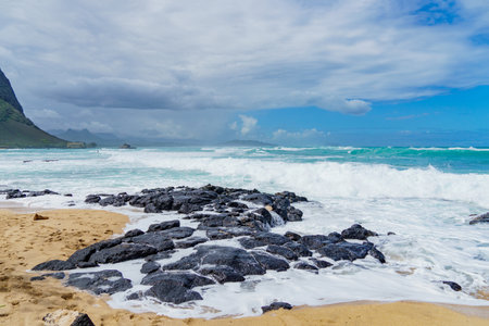 Beach with waves hitting rocks, mountain in backgroundの写真素材