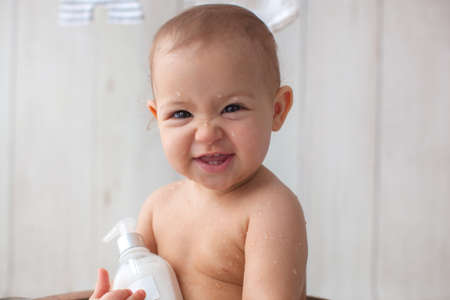 Cute baby girl takes a bath. Basin on wooden backgroun. Clothes are dried on a hanger.
