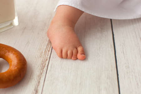 Cute ten months old baby boy, in a suit of a cook, sits on a light wooden background. Kids leg.の写真素材