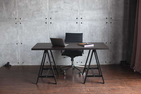 Desktop in the office. Dark concrete walls. Table with laptop and notebook. Office in modern style. の写真素材