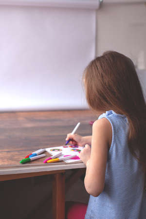 Happy little 7 years girl draws with felt-tip pens. View from above. On wooden table. View from the back.の写真素材