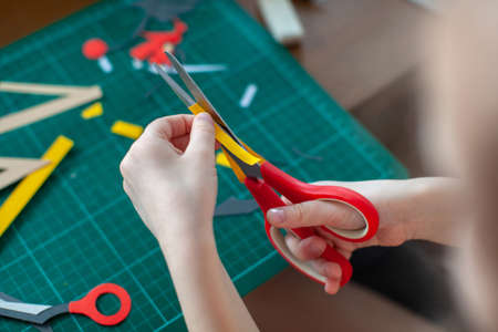 A five-year-old girl cuts out with a scissors yellow paper, craft with kids, cut, hobby, free time.