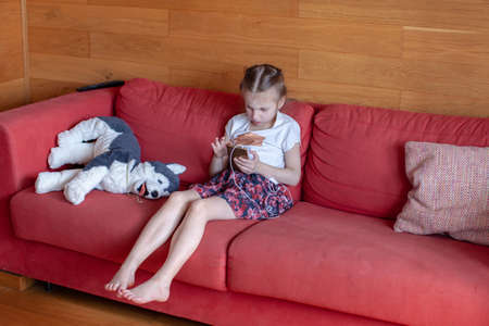 Seven year old girl sitting on the couch and playing on the phone. Home interior.の写真素材