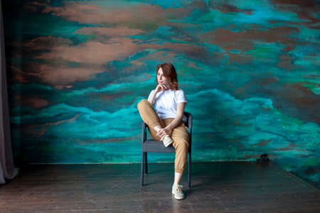 Successful young girl is sitting on a chair. In sneakers, a white T-shirt and sand pants. Watercolor...