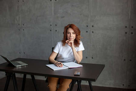A girl in a white T-shirt is sitting at the table. Computer and open notebook. Stay at home concept.の写真素材