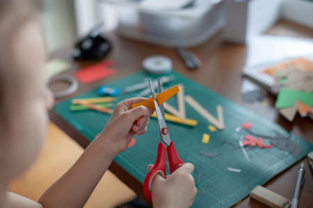 A seven-year-old girl cuts out with a scissors yellow paper. Craft with kids.の写真素材