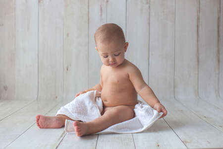 One yeat old baby girl is sitting on wooden backgroun in white towel. After bath time.の写真素材