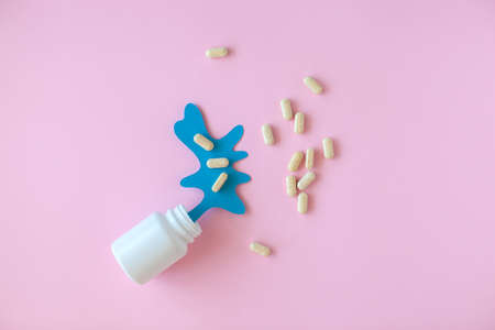 White pill packaging with blue paper splash on pink background. Medicine concept.