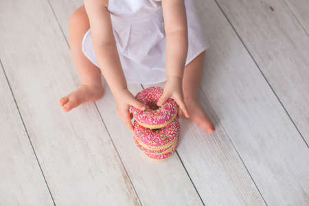 Strawberry donuts with colored sprinkles in the hands of a little girl.の写真素材