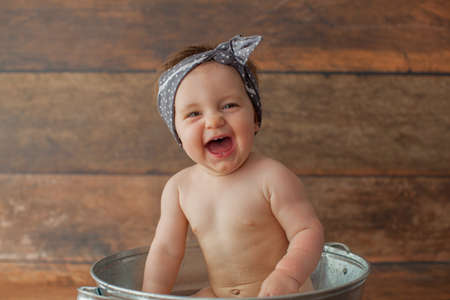 One year old baby girl takes a bath with apricots. She eats cherry. Dark wooden background.