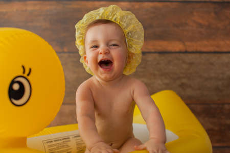 One year old baby girl takes a bath. With yellow duck. First birthday decoration for photoshoot. Shower cap on her head.の写真素材