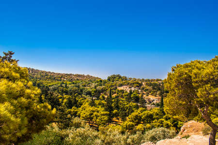 Stunning view of a valley surrounded by mountains, with green trees and a beautiful blue sky with a few cloudsの写真素材