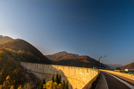 Beautiful view of a dam seen from up high, surrounded by forests and colored trees, in a sunny day...