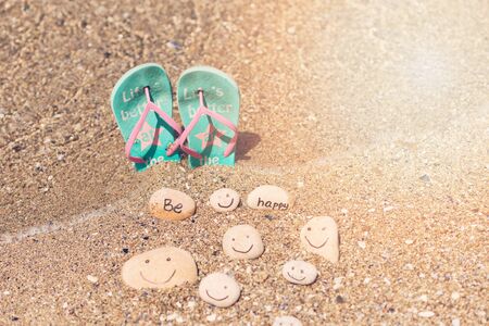 Beautiful sunlight with clean sea sand and the waves are blowing on the beach. Flip flops and small rocks with inscription, near the water.の写真素材