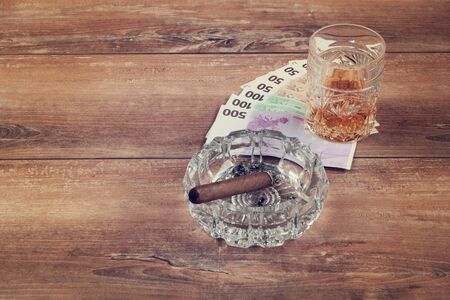 Glass of whiskey and a money with cuban cigar on a brown wooden table. Top view.の写真素材