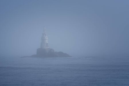 Lighthouse Along Rocky Coastline on Foggy Morningの写真素材